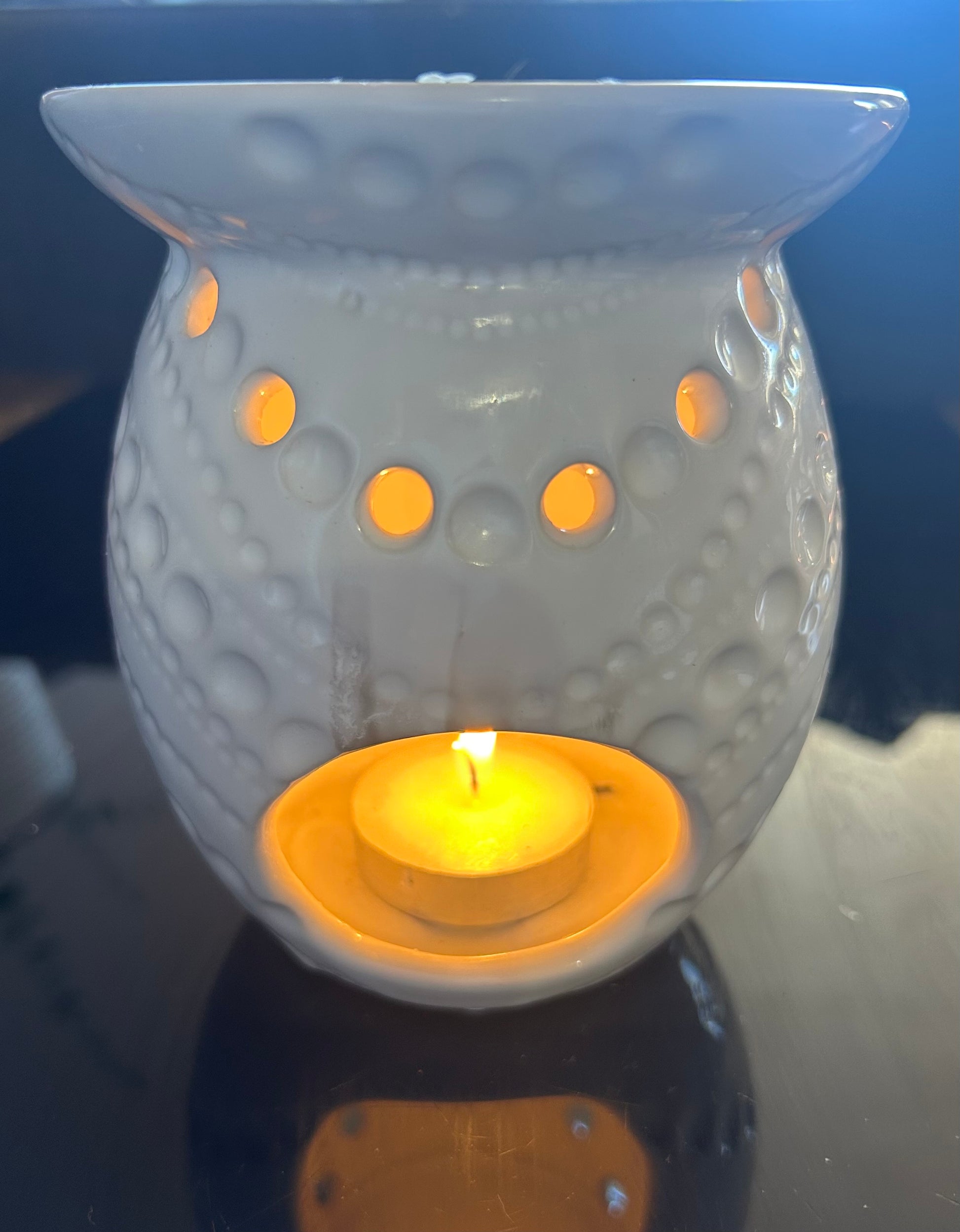 White wax warmer with a lit candle inside on a dark surface
